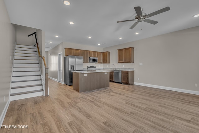 kitchen with light stone countertops, a kitchen island, light wood-type flooring, appliances with stainless steel finishes, and ceiling fan