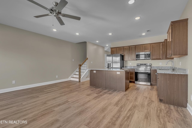 kitchen featuring light stone countertops, light hardwood / wood-style flooring, a center island, stainless steel appliances, and ceiling fan