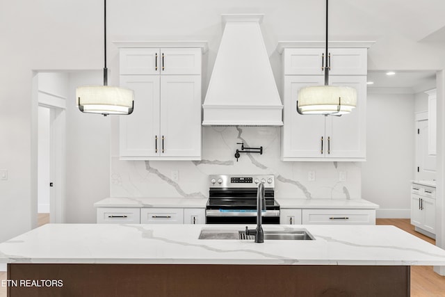 kitchen with custom exhaust hood, electric stove, an island with sink, pendant lighting, and white cabinets