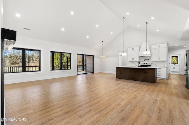 kitchen with pendant lighting, an island with sink, light wood-type flooring, backsplash, and white cabinets