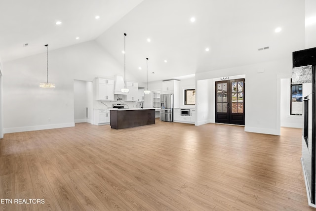 unfurnished living room featuring light wood-type flooring, french doors, and high vaulted ceiling