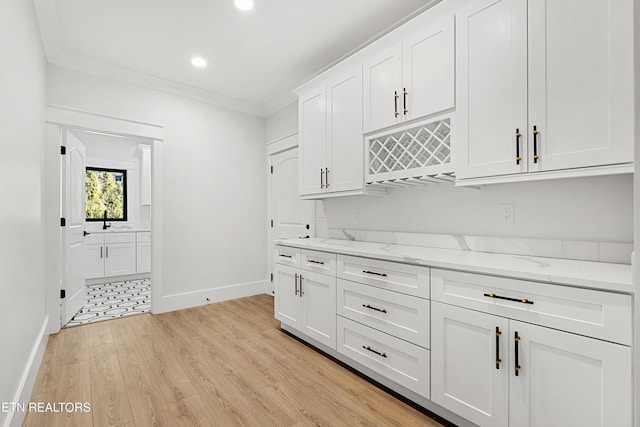 kitchen featuring light stone counters, light hardwood / wood-style floors, crown molding, white cabinetry, and sink