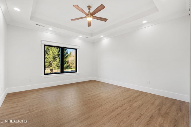 empty room featuring crown molding, ceiling fan, a tray ceiling, and light wood-type flooring