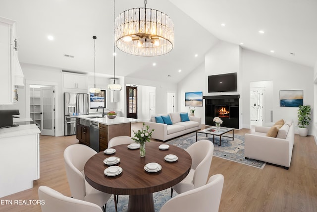 dining area with light hardwood / wood-style flooring, a tile fireplace, a notable chandelier, high vaulted ceiling, and sink