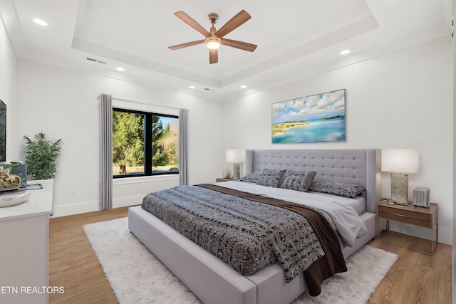 bedroom with ceiling fan, a tray ceiling, crown molding, and light hardwood / wood-style floors