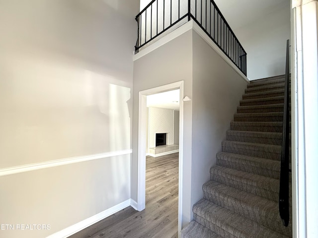 stairs with a high ceiling, a fireplace, and wood-type flooring