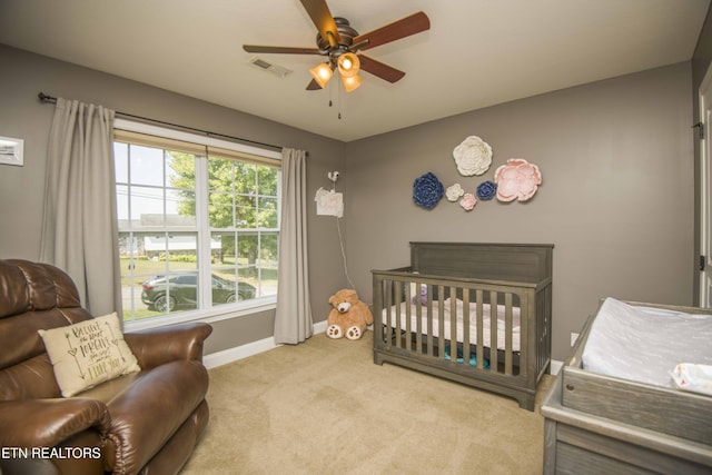 bedroom with a nursery area, light carpet, and ceiling fan