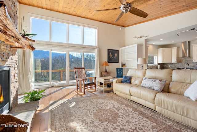 living room featuring a fireplace, ceiling fan, a mountain view, and wood ceiling