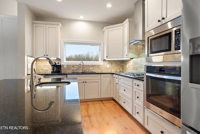 kitchen featuring dark stone counters, appliances with stainless steel finishes, wall chimney exhaust hood, and white cabinetry