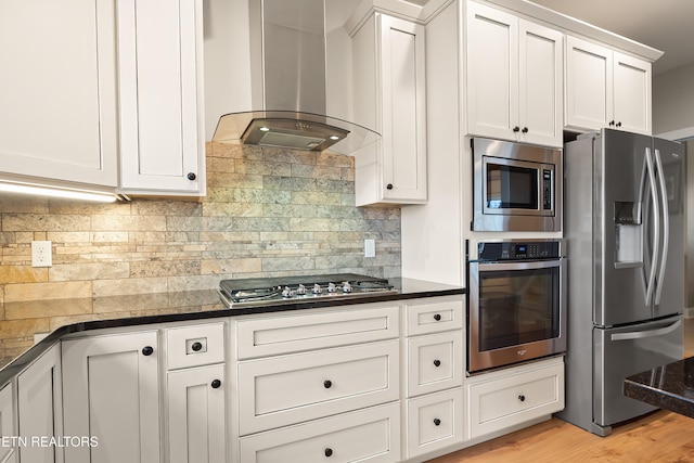 kitchen featuring stainless steel appliances, white cabinetry, wall chimney exhaust hood, light hardwood / wood-style floors, and tasteful backsplash