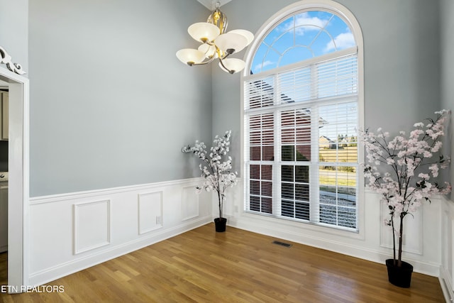 unfurnished dining area featuring a wainscoted wall, a notable chandelier, wood finished floors, and visible vents