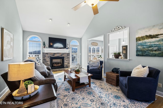 living room featuring a stone fireplace, wood finished floors, baseboards, and high vaulted ceiling