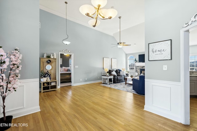 living room with light wood-style floors, wainscoting, a fireplace, and ceiling fan with notable chandelier