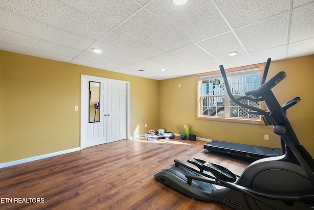 exercise area with a drop ceiling, recessed lighting, baseboards, and wood finished floors