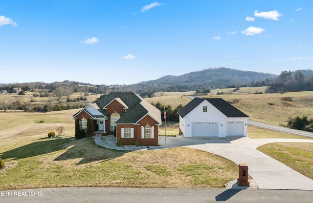 view of front of house with a rural view, a mountain view, concrete driveway, and a front lawn