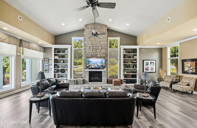 living area with high vaulted ceiling, a stone fireplace, wood finished floors, and a ceiling fan