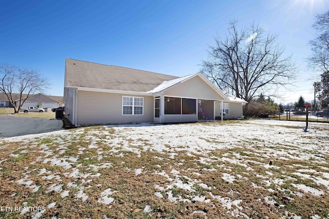 snow covered rear of property featuring a sunroom