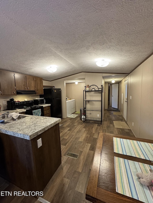 kitchen featuring sink, vaulted ceiling, dark hardwood / wood-style floors, washing machine and dryer, and black appliances