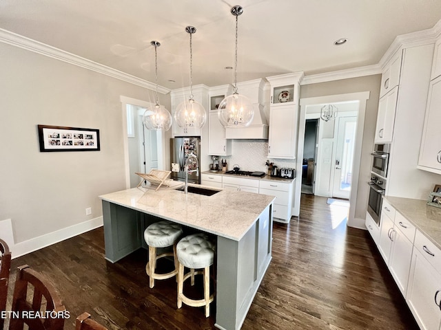 kitchen featuring white cabinetry, light stone countertops, premium range hood, hanging light fixtures, and a kitchen island with sink