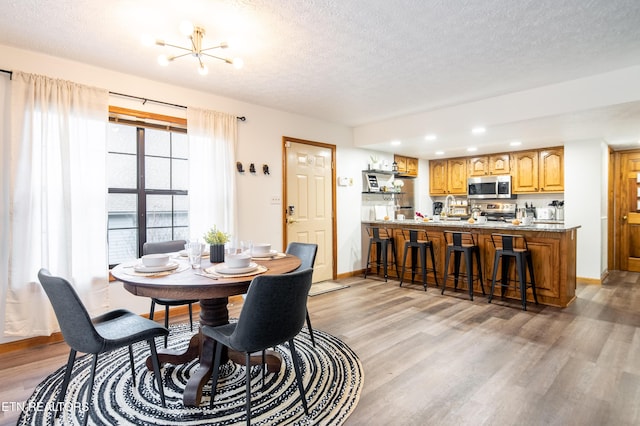 dining space with an inviting chandelier, a textured ceiling, and light wood-type flooring