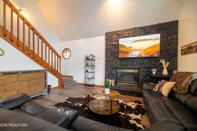 living room featuring vaulted ceiling, a stone fireplace, and light wood-type flooring