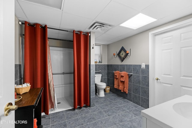 bathroom with toilet, a paneled ceiling, vanity, a shower with curtain, and tile walls