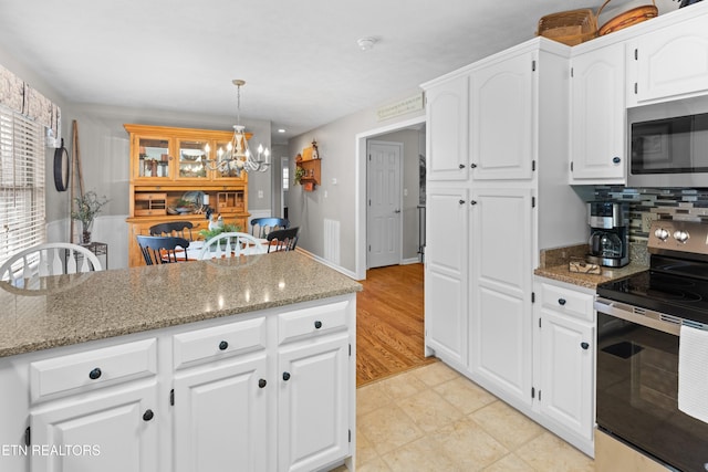 kitchen with stainless steel appliances, hanging light fixtures, light stone counters, white cabinets, and an inviting chandelier