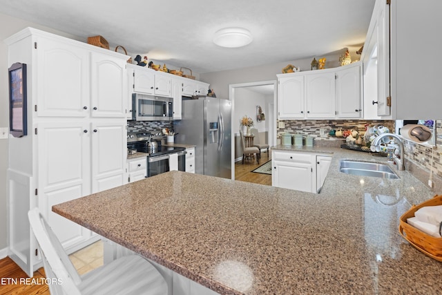 kitchen with white cabinets, a kitchen breakfast bar, kitchen peninsula, backsplash, and appliances with stainless steel finishes