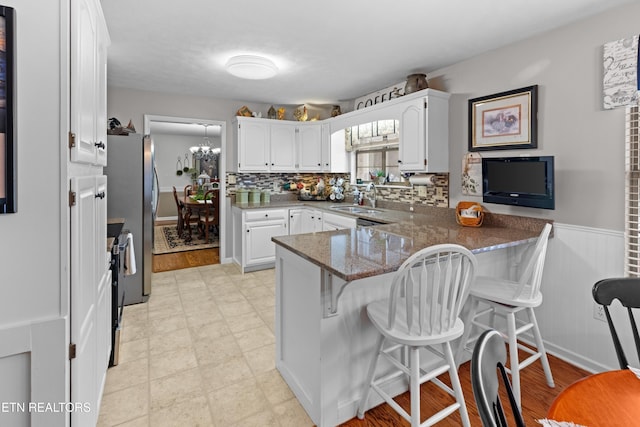 kitchen with kitchen peninsula, a kitchen bar, white cabinetry, dark stone counters, and sink