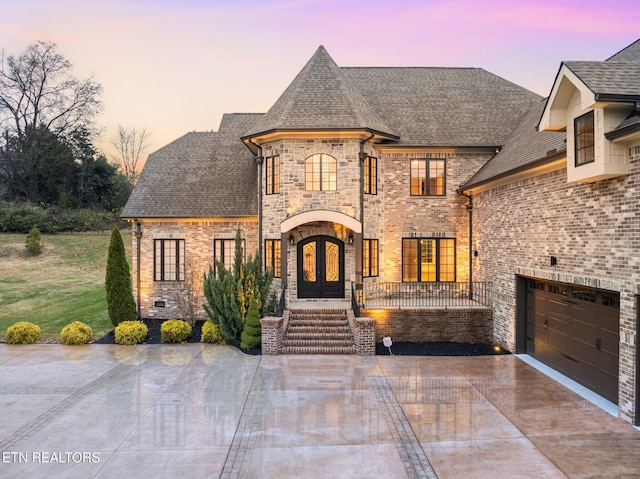 french country style house with a garage, a shingled roof, concrete driveway, french doors, and brick siding