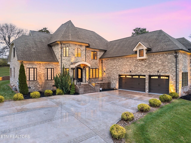 french country style house featuring concrete driveway, a shingled roof, a lawn, and brick siding