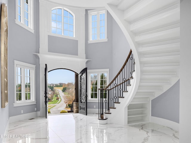 foyer entrance with visible vents, a towering ceiling, stairs, marble finish floor, and baseboards