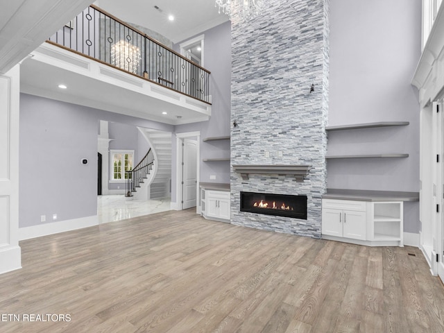 unfurnished living room with a high ceiling, light hardwood / wood-style flooring, crown molding, and a stone fireplace