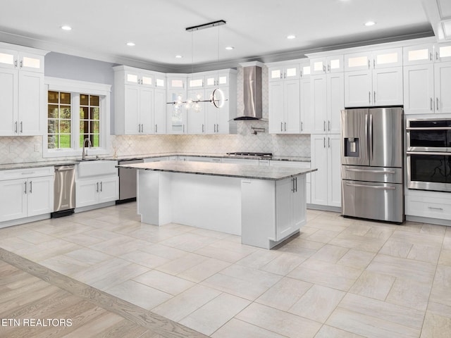 kitchen with stainless steel appliances, white cabinets, light stone counters, hanging light fixtures, and wall chimney range hood