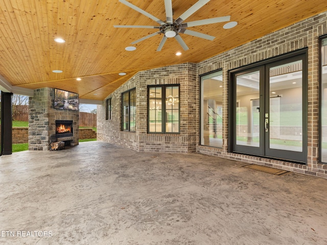 unfurnished living room featuring brick wall, ceiling fan, wood ceiling, and an outdoor stone fireplace