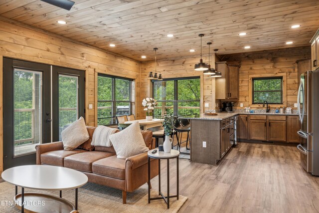 living room with a wealth of natural light, light hardwood / wood-style floors, wooden ceiling, and wooden walls