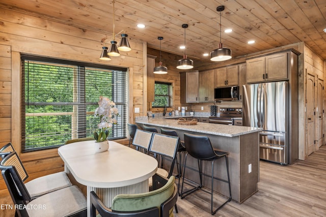 kitchen with stainless steel appliances, kitchen peninsula, wood walls, light stone countertops, and pendant lighting