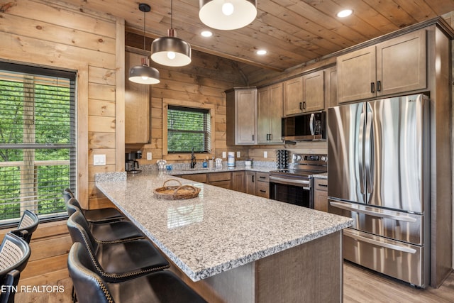 kitchen with wooden ceiling, wood walls, stainless steel appliances, light stone countertops, and decorative light fixtures