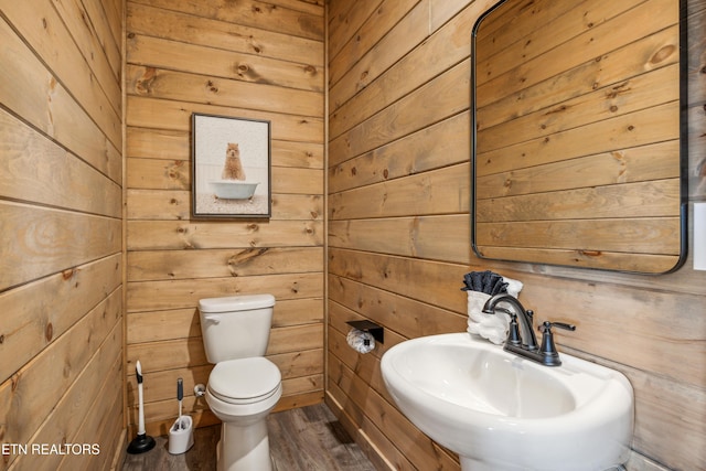 bathroom with sink, wood-type flooring, wooden walls, and toilet