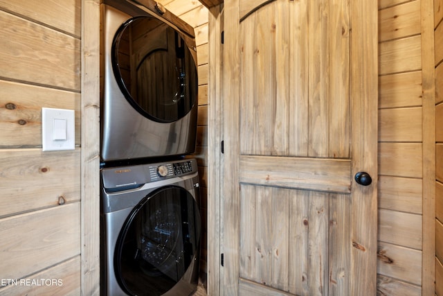 clothes washing area with stacked washer / drying machine and wooden walls