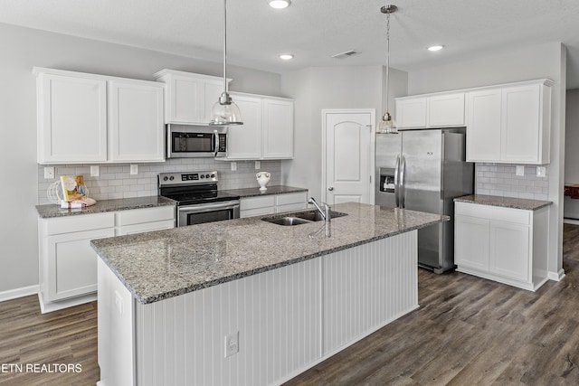 kitchen featuring stainless steel appliances, white cabinetry, hanging light fixtures, and an island with sink