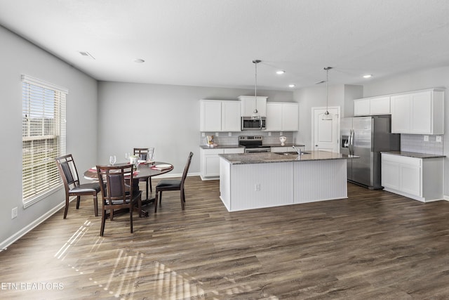 kitchen with a kitchen island with sink, hanging light fixtures, dark wood-type flooring, appliances with stainless steel finishes, and white cabinets