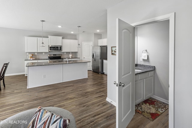 kitchen featuring appliances with stainless steel finishes, backsplash, pendant lighting, white cabinets, and a kitchen island with sink