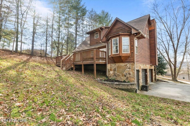 rear view of property with a garage, stone siding, a wooden deck, and driveway