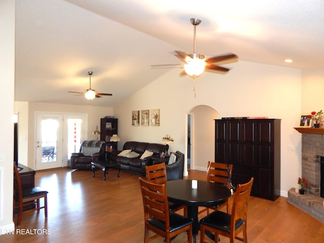 dining space featuring ceiling fan, vaulted ceiling, a fireplace, hardwood / wood-style floors, and french doors