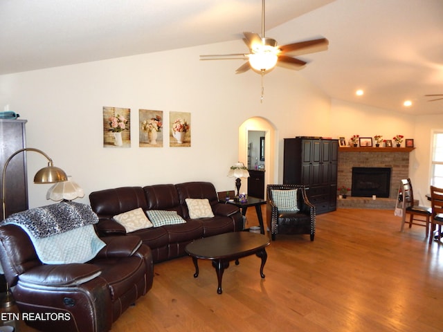 living room featuring ceiling fan, lofted ceiling, a fireplace, and wood-type flooring