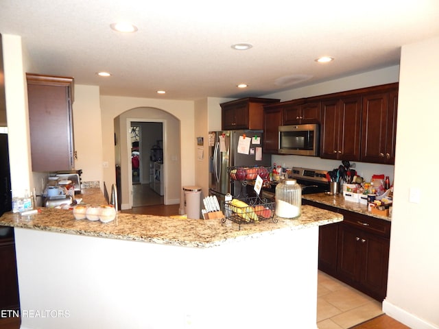 kitchen featuring light tile patterned floors, kitchen peninsula, appliances with stainless steel finishes, and light stone counters