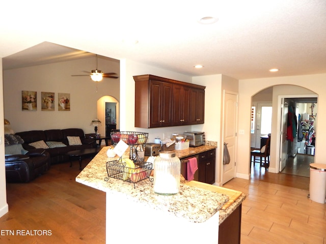 kitchen with ceiling fan, light stone counters, kitchen peninsula, and light wood-type flooring