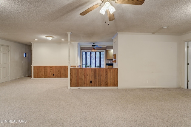 unfurnished living room with wood walls, light carpet, ceiling fan, ornamental molding, and a textured ceiling