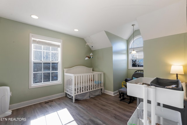 bedroom featuring dark wood-type flooring, a crib, and vaulted ceiling